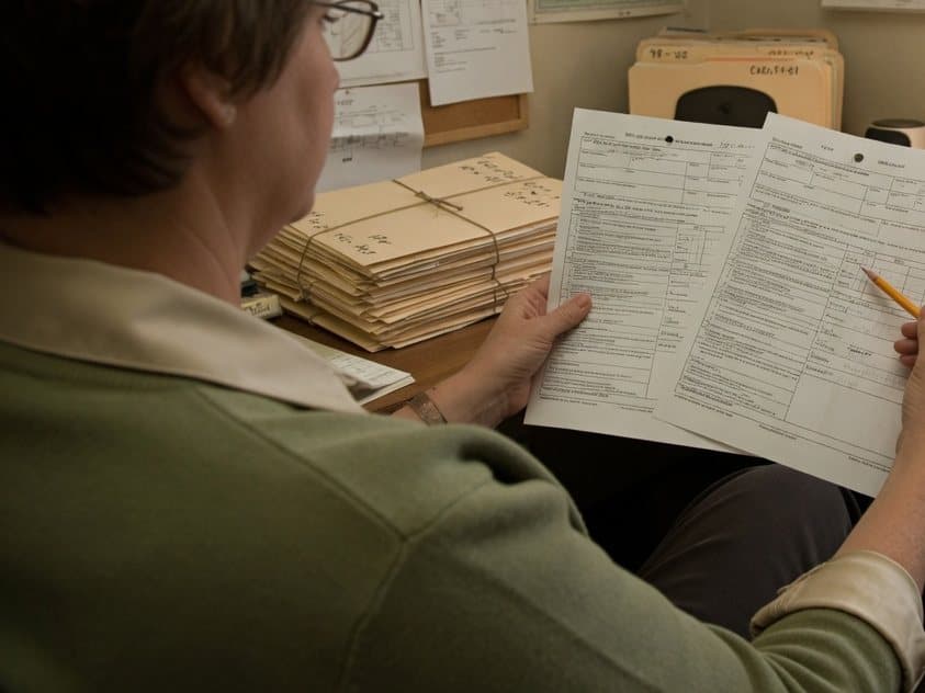 An office manager comparing two printed versions of the same form, pencil in hand