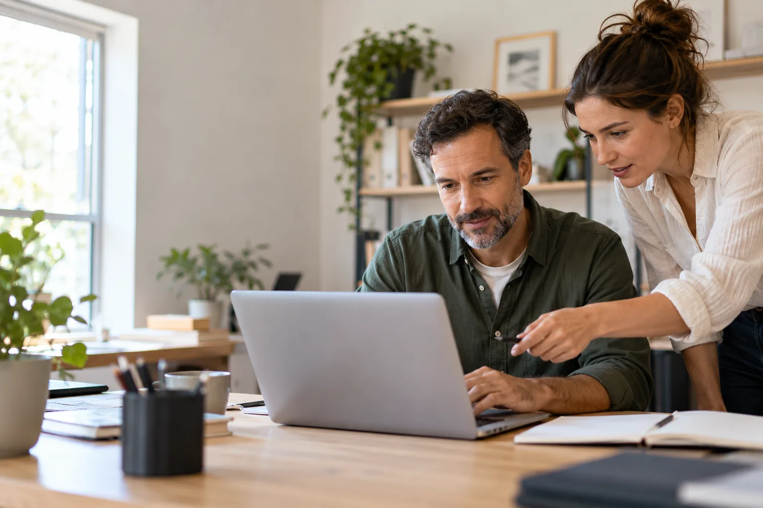 Two coworkers review a laptop together at a desk.